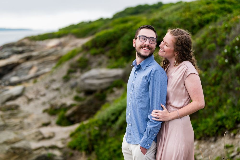 A couple shares romantic moments on the rocky coastal cliffs surrounded by green vegetation and ocean views.
