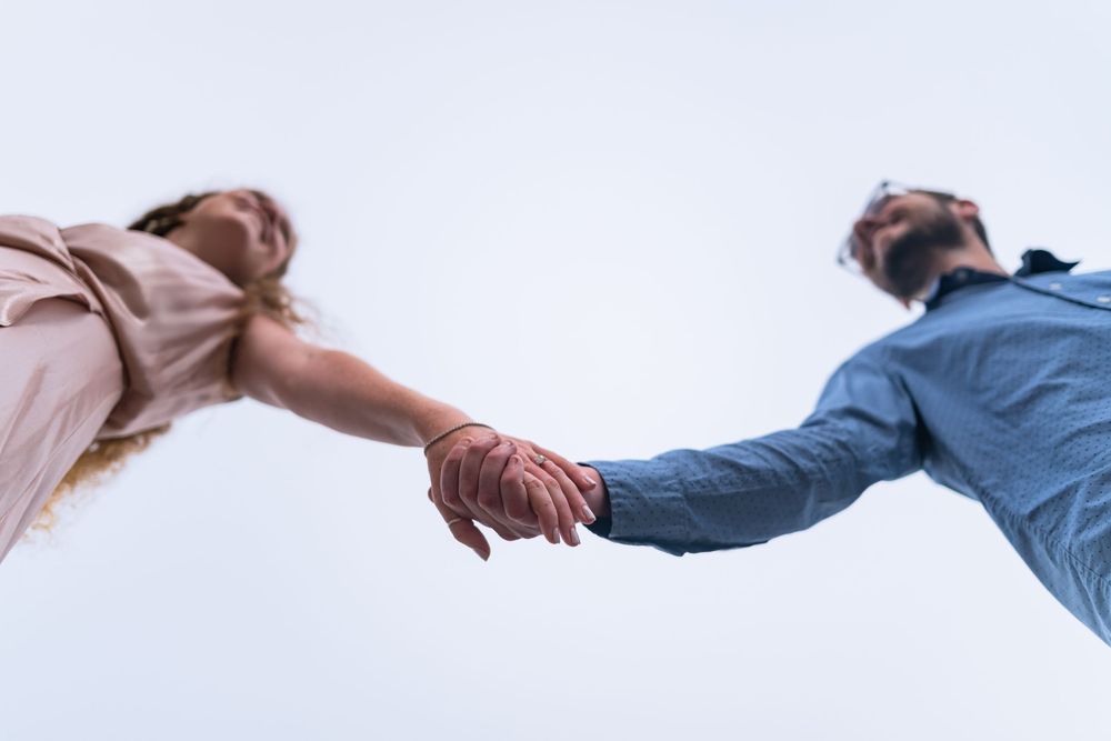 Low angle view of two people holding hands against a bright sky background.