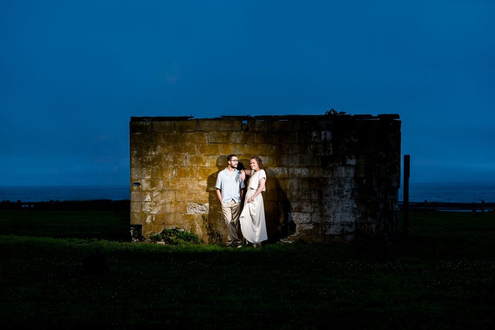 Silhouettes of a romantic couple stand in a doorway of a stone structure against a blue evening sky.