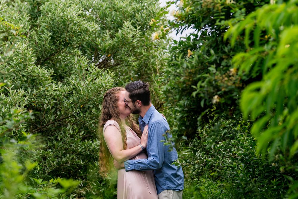 A romantic couple embraces in a lush green garden setting during a warm summer day.