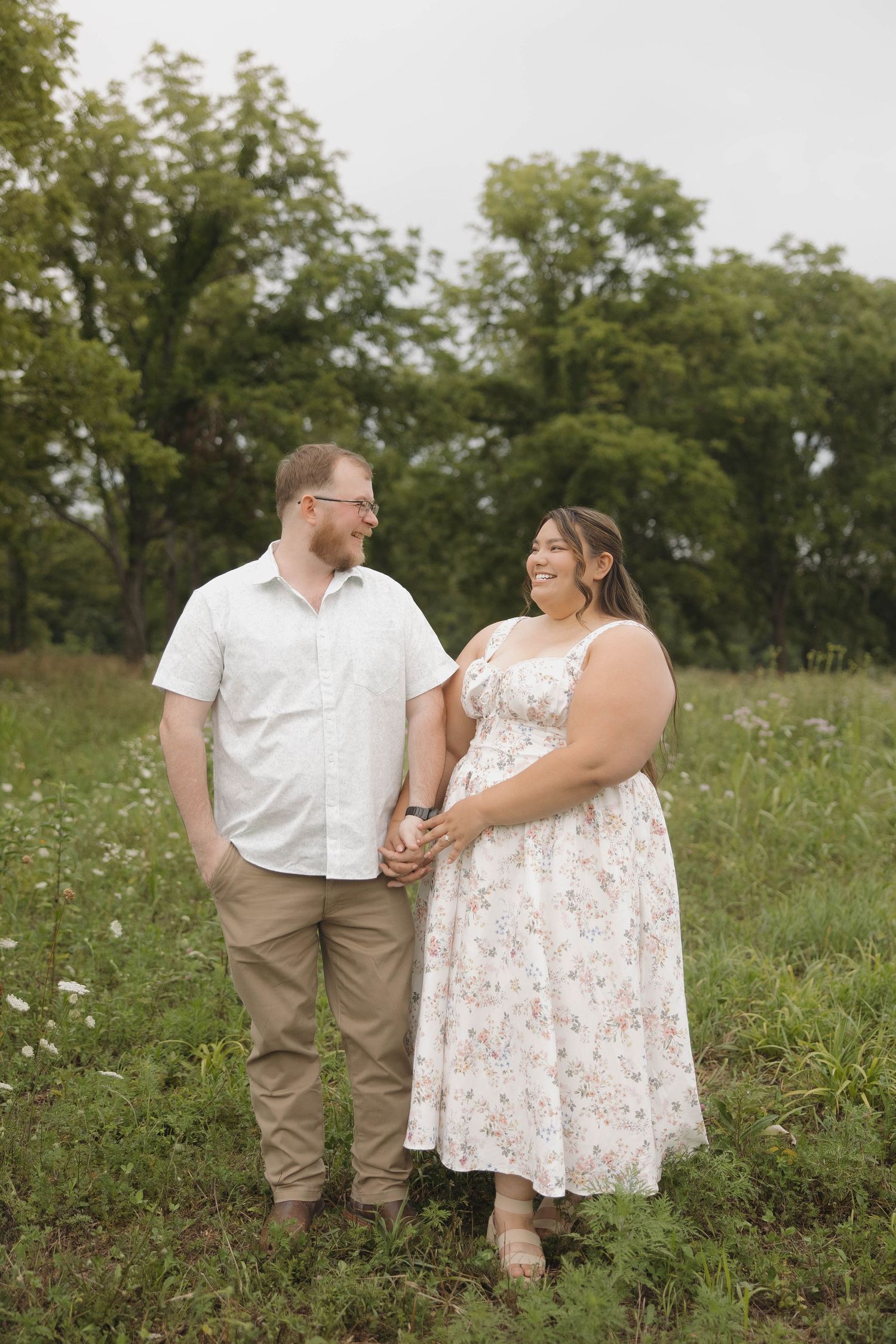 A couple in coordinated white and khaki outfits share romantic moments together in a wildflower meadow during a summer photo shoot.