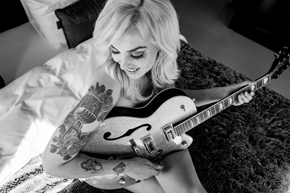 Monochrome closeup of guitar player with tattoos holding silver electric guitar.
