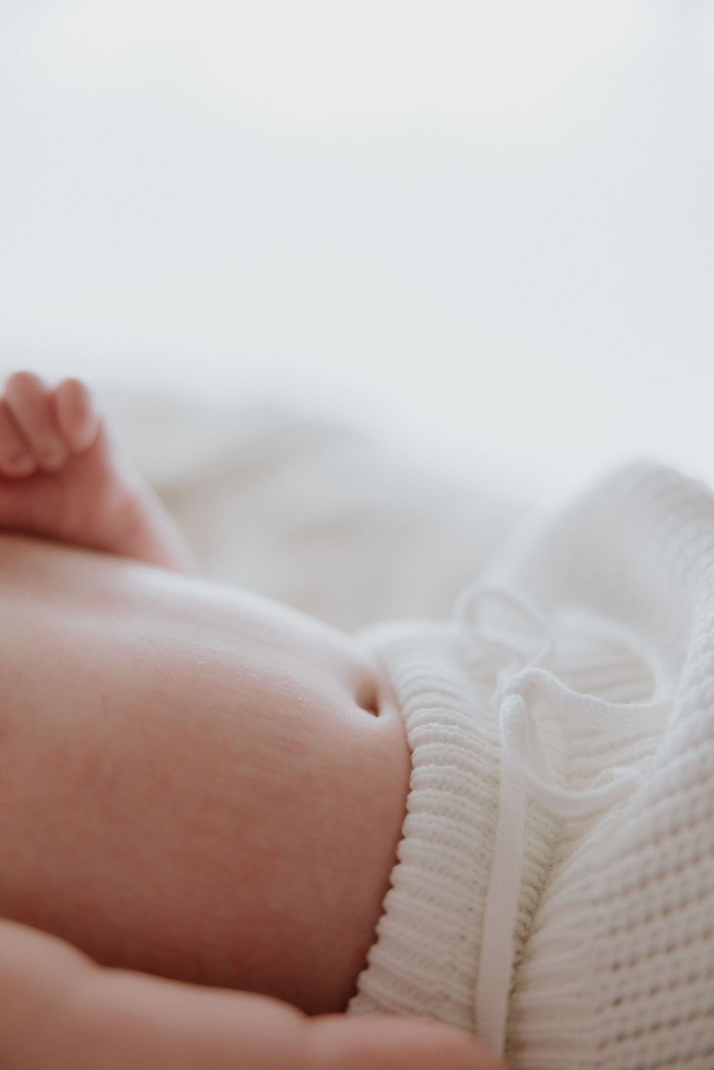 Close-up view of a tiny baby hand reaching up while wearing a soft white knit sweater.
