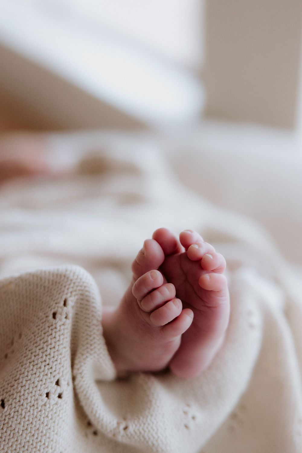 Close-up view of tiny newborn baby foot wrapped in soft knitted white blanket with delicate eyelet pattern details.