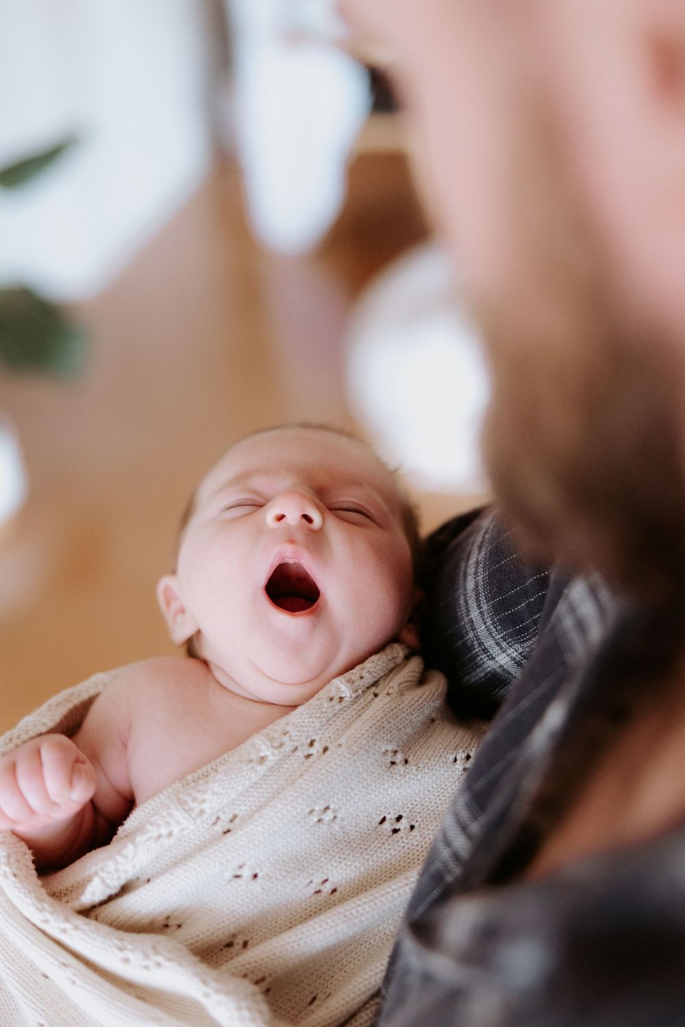 Sequence of photos showing a sleeping baby yawning and waking up gently in soft lighting and blankets.