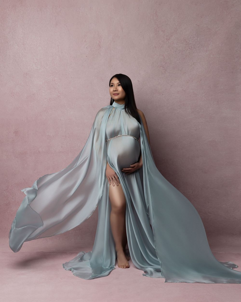 A flowy dusty blue fabric dress creates an ethereal movement sequence against a muted pink backdrop with dramatic poses.