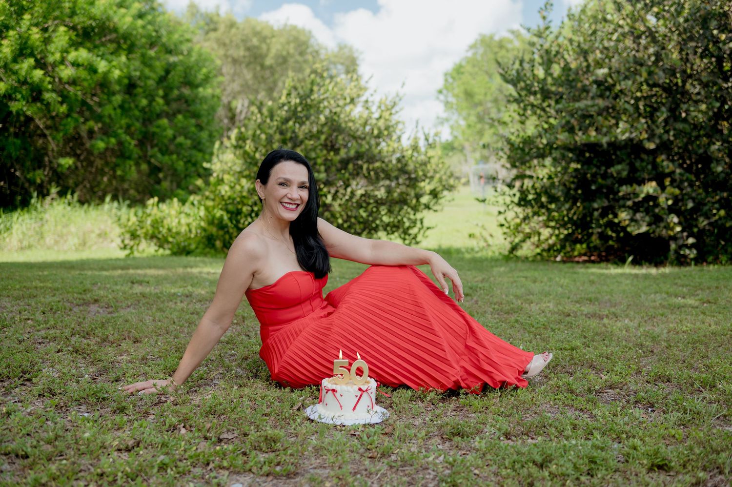 Woman in flowing red maternity dress poses gracefully on grassy hill during outdoor photo session.