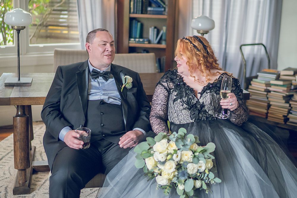 A wedding couple shares a tender moment while sitting on an elegant sofa surrounded by beautiful floral arrangements.