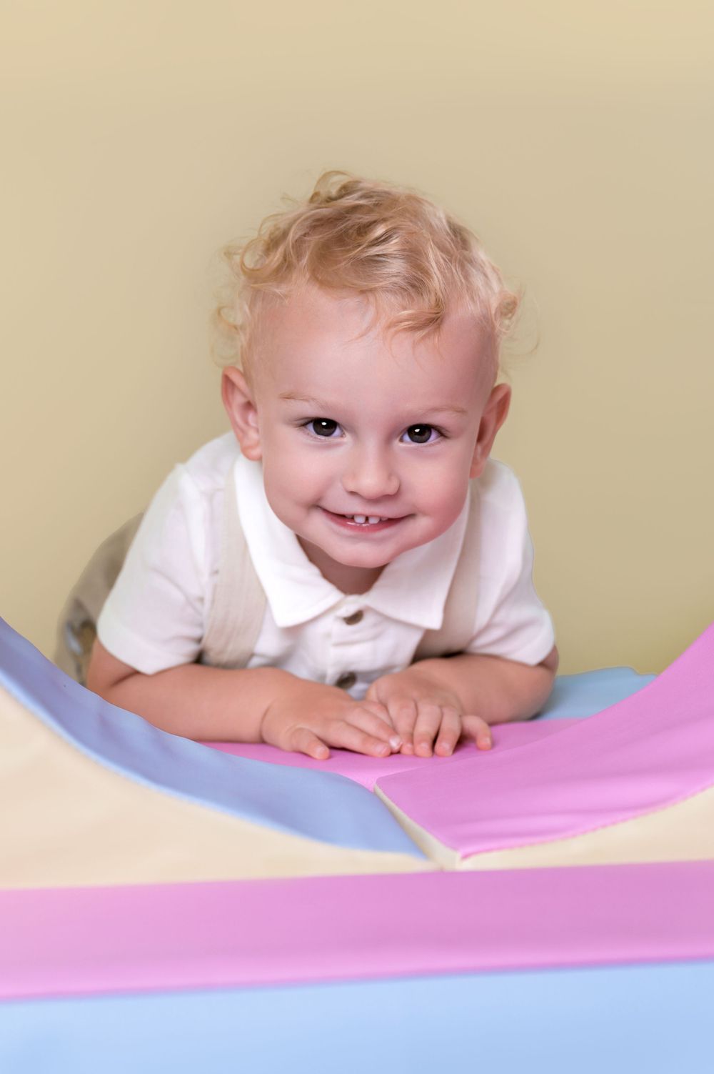 Young child in white polo shirt smiles while leaning on colorful fabric background.