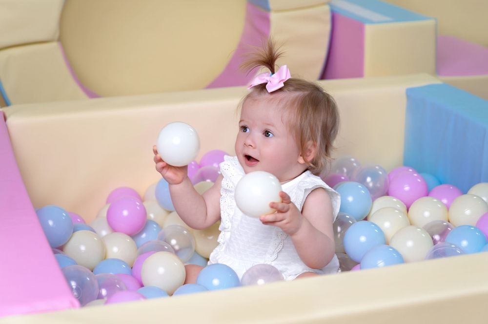 A small child plays in a colorful ball pit filled with pastel blue, white and purple plastic balls.