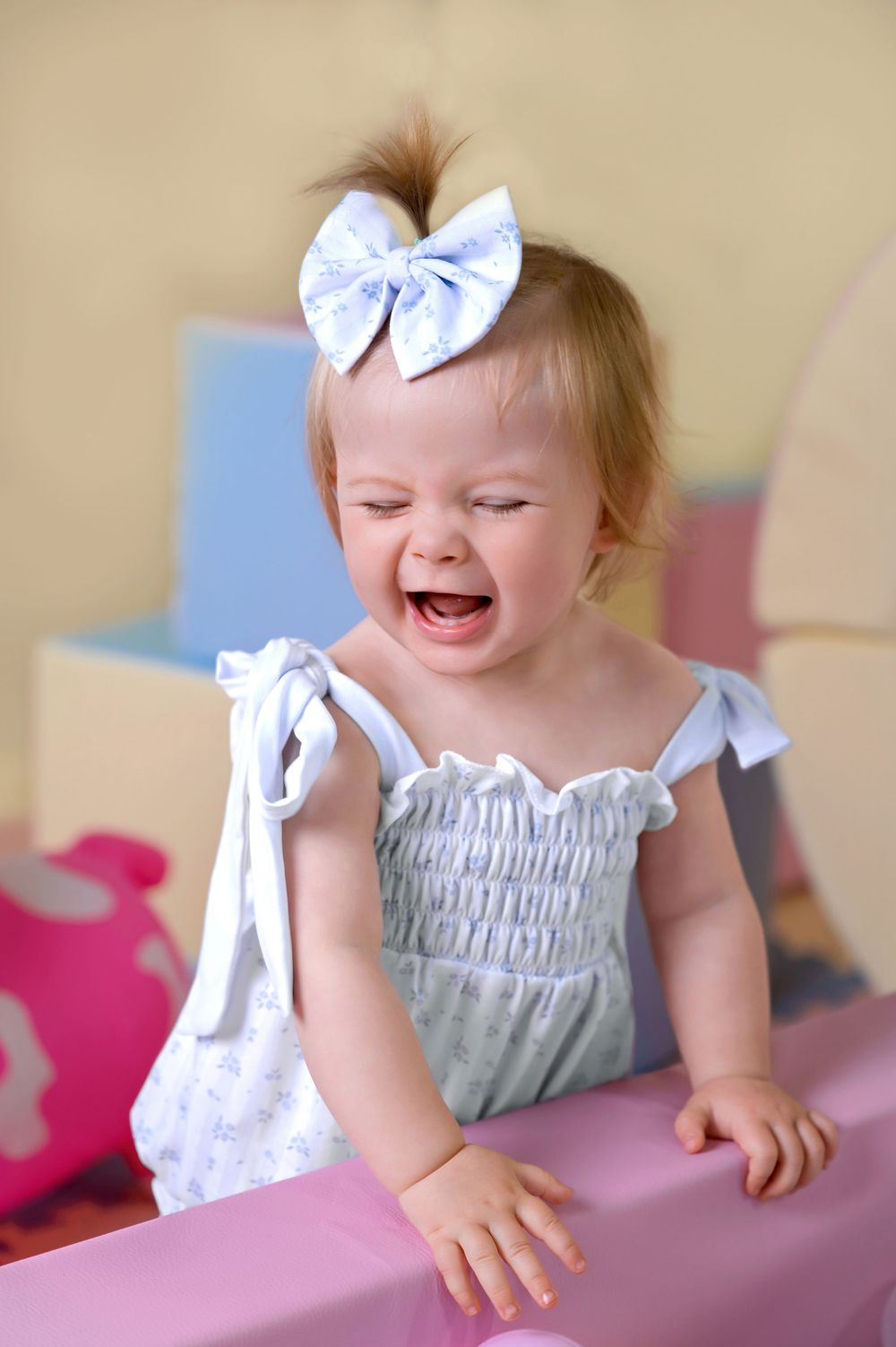 A baby wearing a grey ruffled dress and white hair bow laughs joyfully in sequence of candid moments.