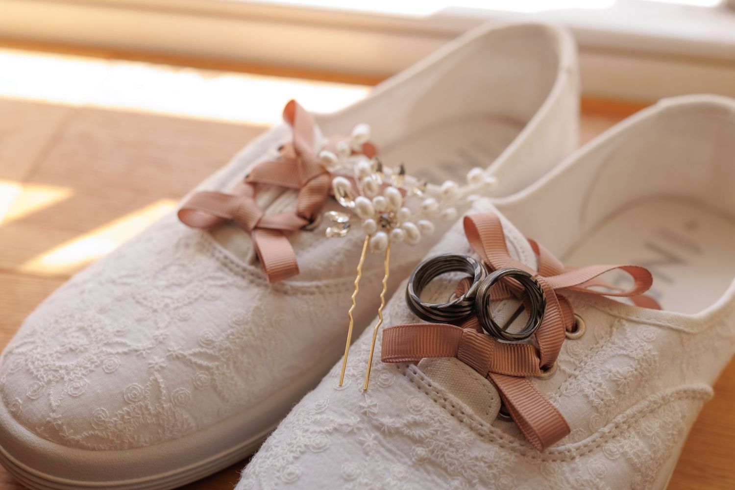 White lace wedding shoes with pink satin ribbons displayed on a neutral background.