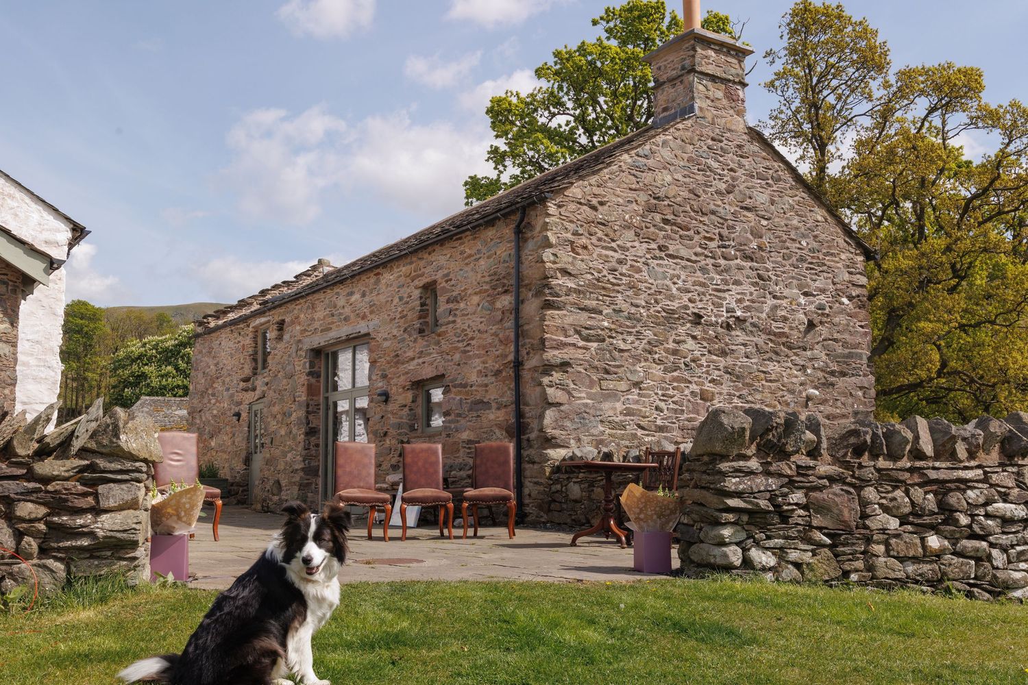 Rustic stone cottage with slate roof nestled among autumn trees in rural countryside setting.
