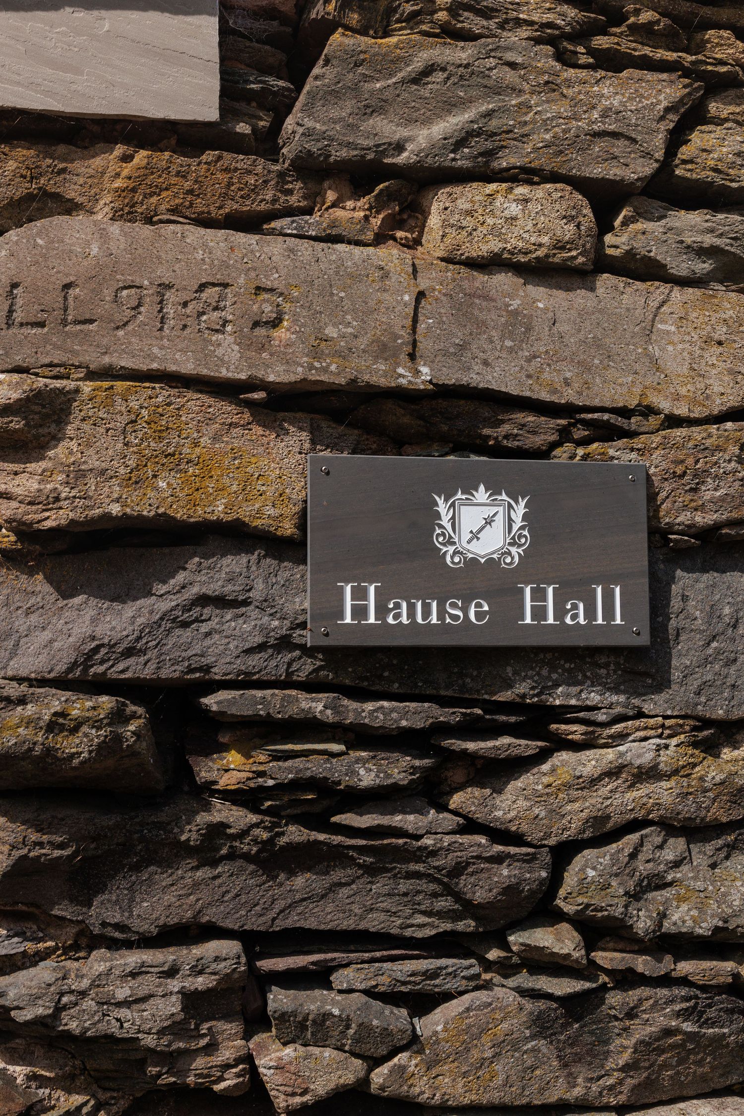 Black and white Hause Hall name plate mounted on rustic stone wall with layered rock texture.