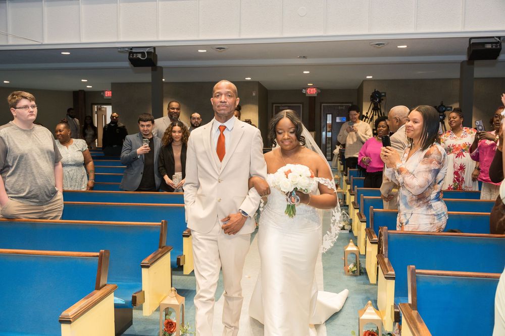 A bride and groom walk down the aisle in a church with bright blue carpeting as guests look on during the ceremony.