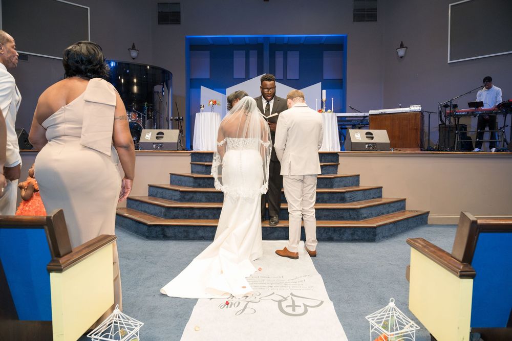 A wedding ceremony taking place at a church altar with a long white aisle runner decorated with floral designs.