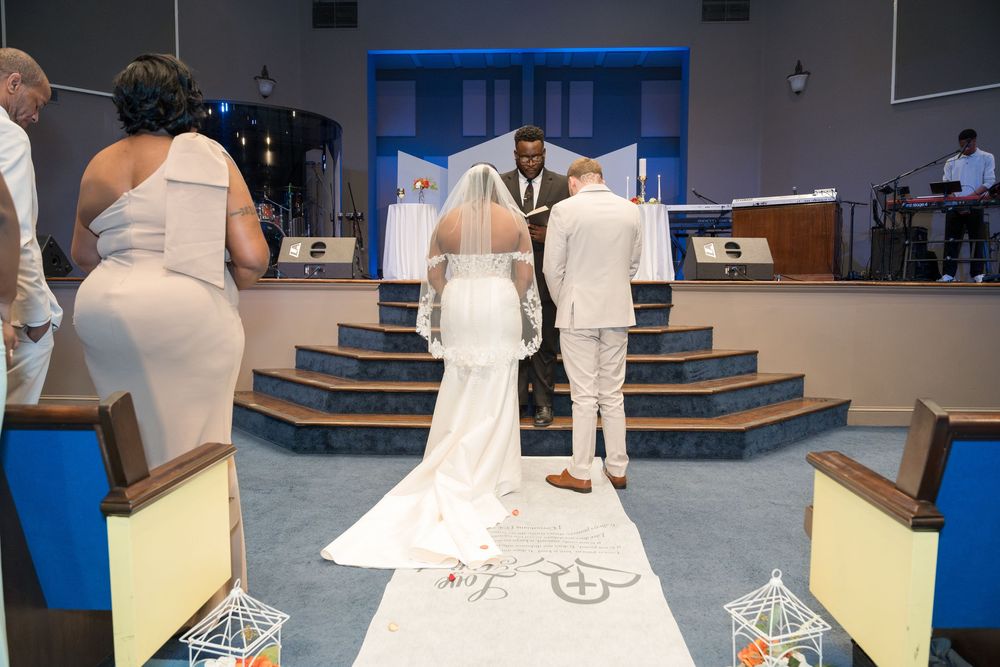A wedding ceremony takes place inside a modern church sanctuary with blue lighting and multiple attendees.