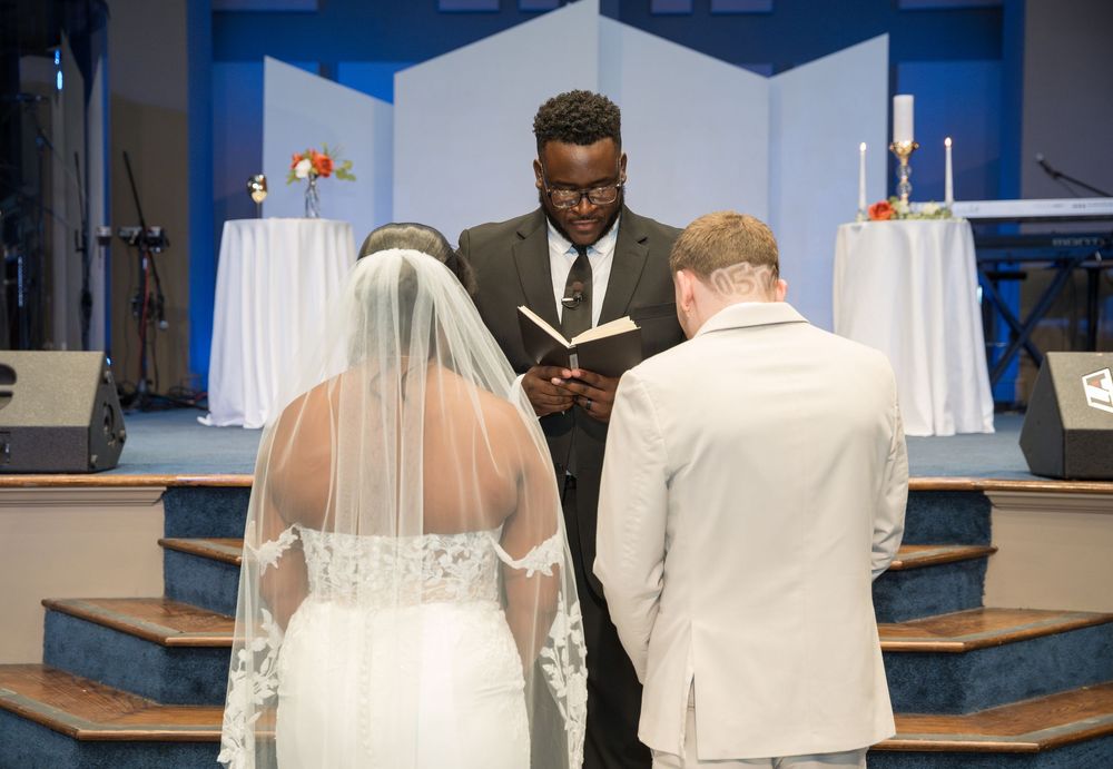 A wedding ceremony takes place at the altar of a church with a couple facing the officiant during their vows.