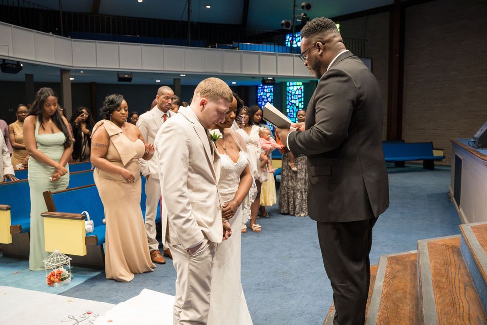A group stands in formation wearing tan and white attire inside a church or auditorium while interacting with a speaker.