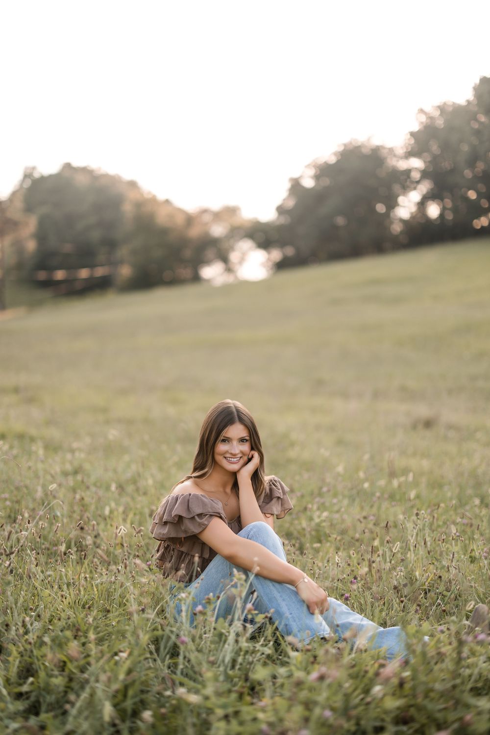 Person in blue jeans sitting in a grassy meadow during golden hour sunset.