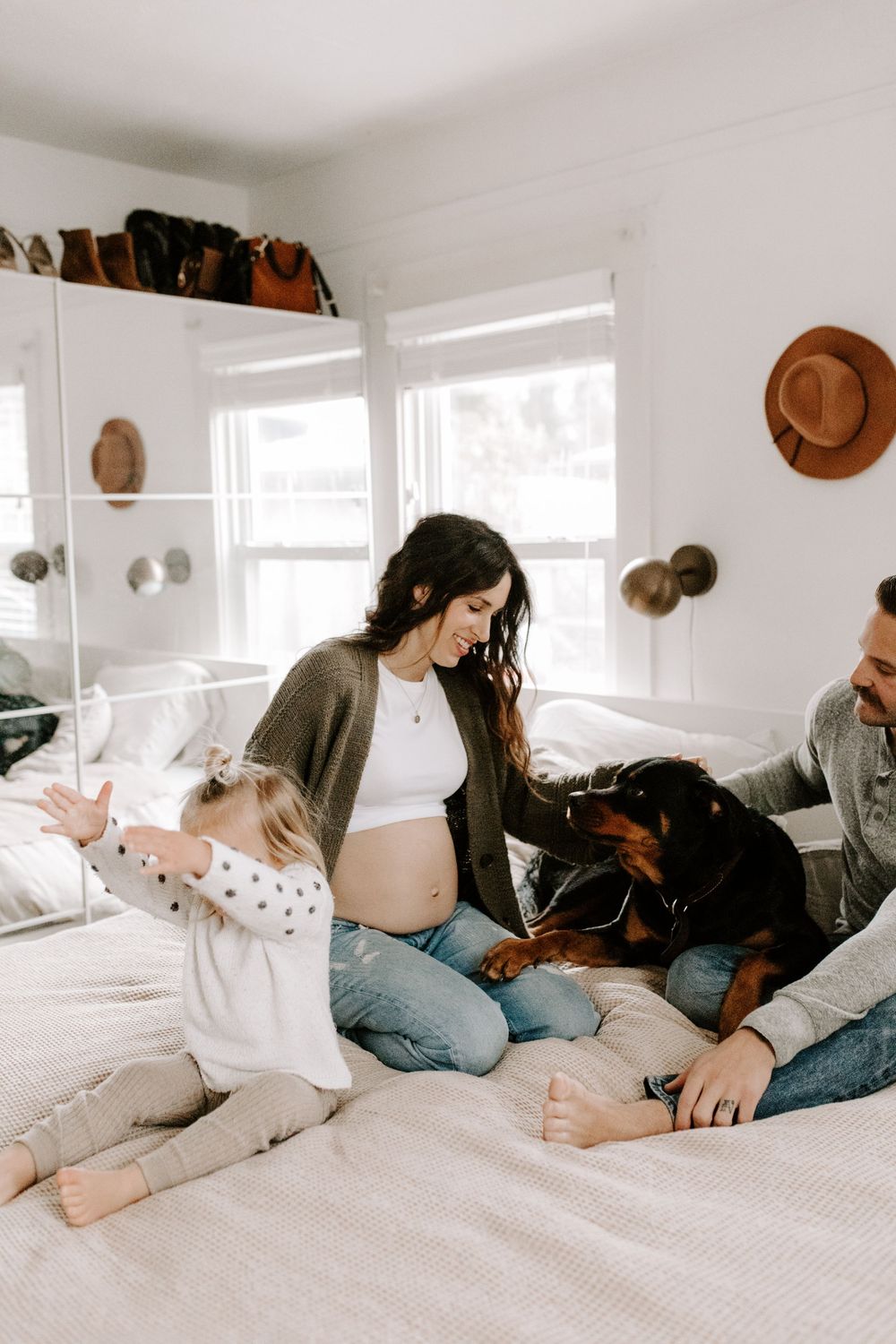A cozy family scene on a bed with a pregnant woman, child, and happy dog.