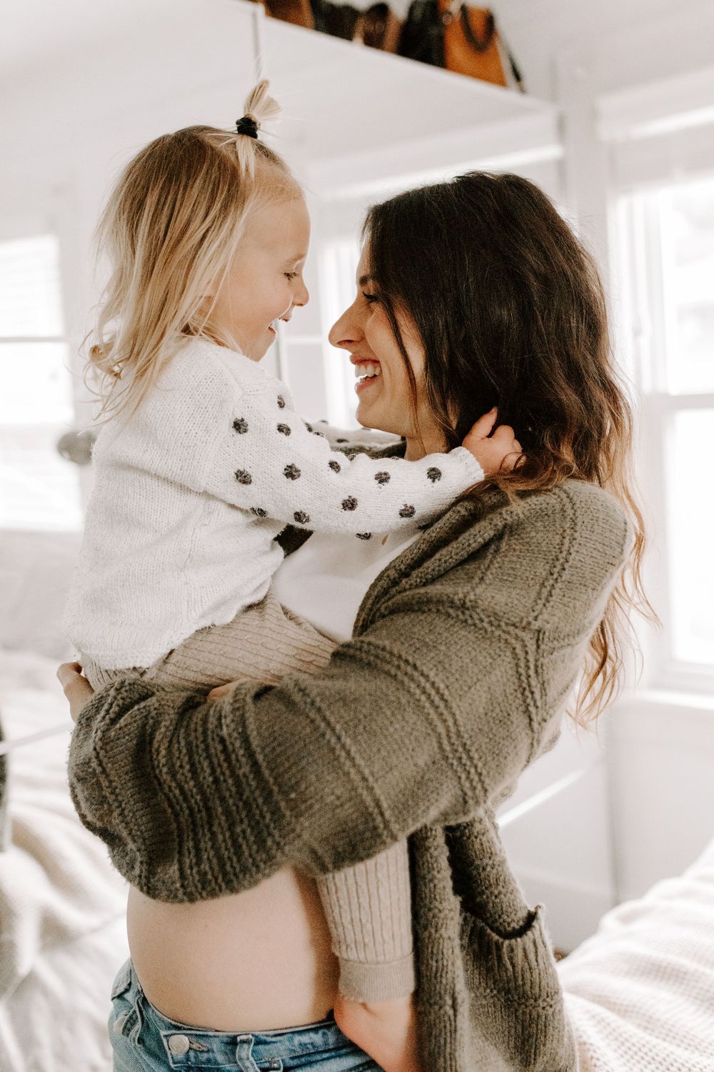 A joyful embrace between mother and child on a bright white bed.