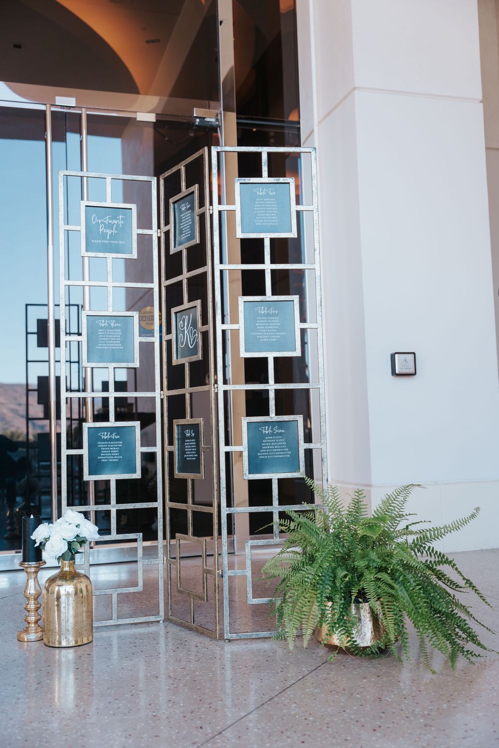 Modern hotel hallway features geometric mirrored wall art with blue panels and decorative potted ferns on a polished floor.