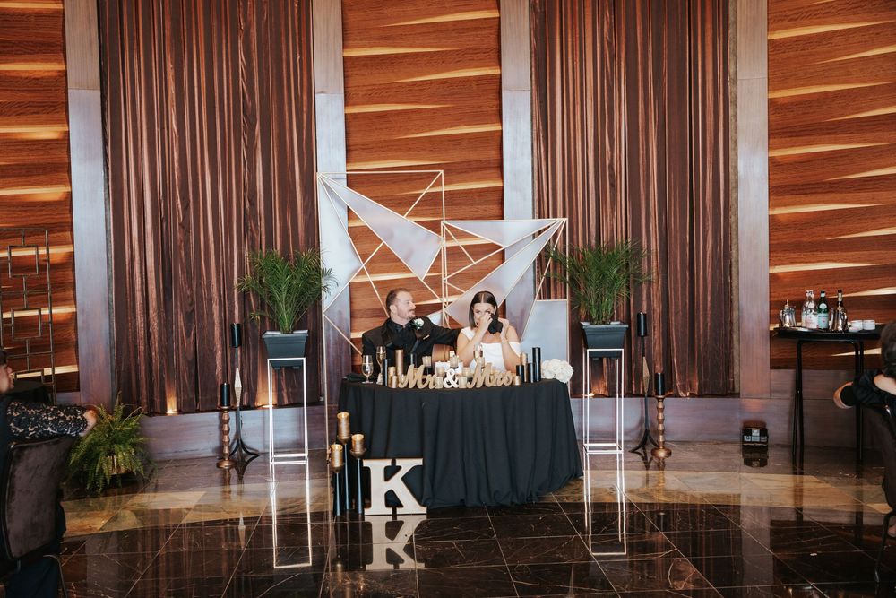 Modern wedding reception setup with a black sweetheart table decorated with white origami accents and monogram letters.