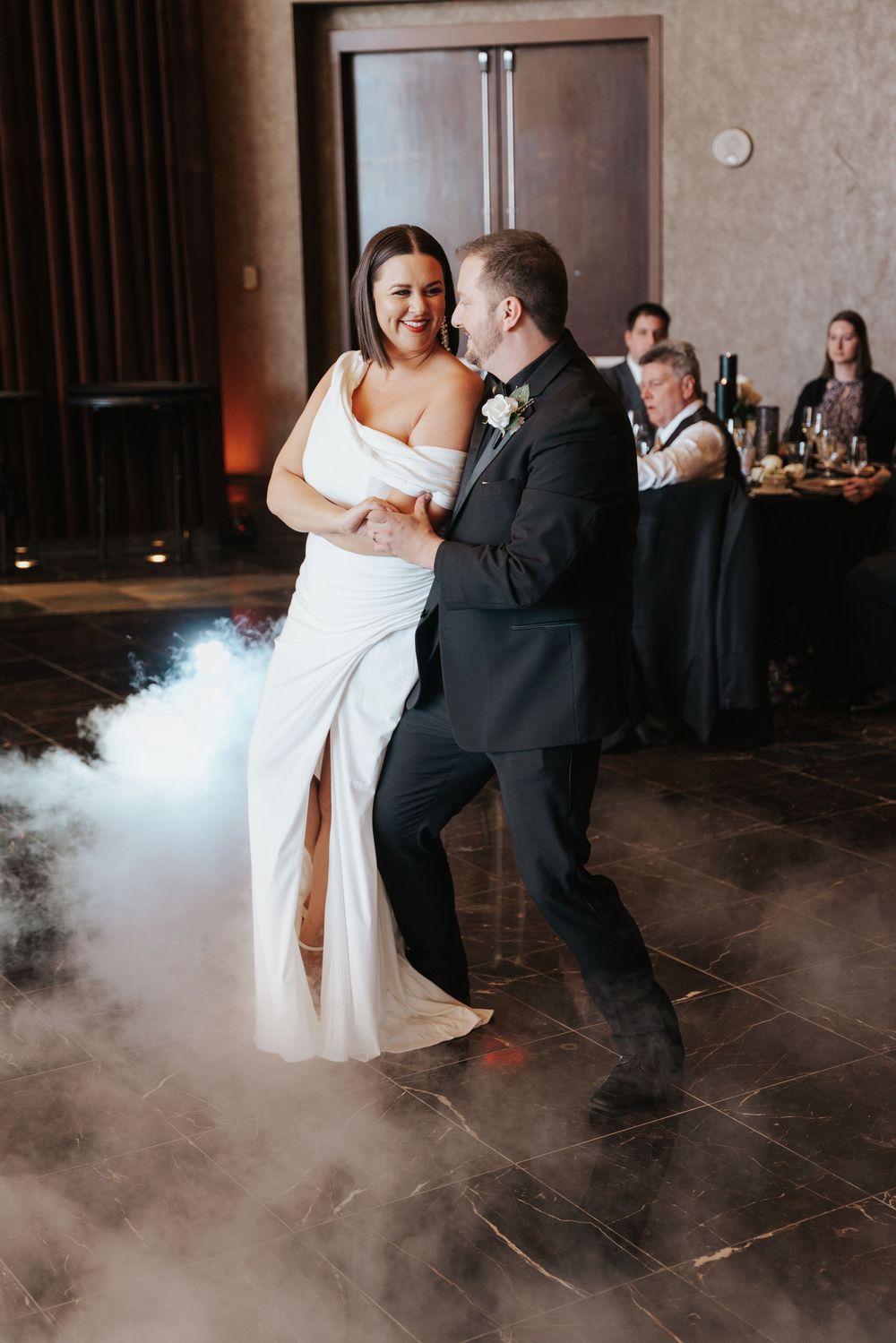 A couple shares their first dance as newlyweds on a misty dance floor at their wedding reception.
