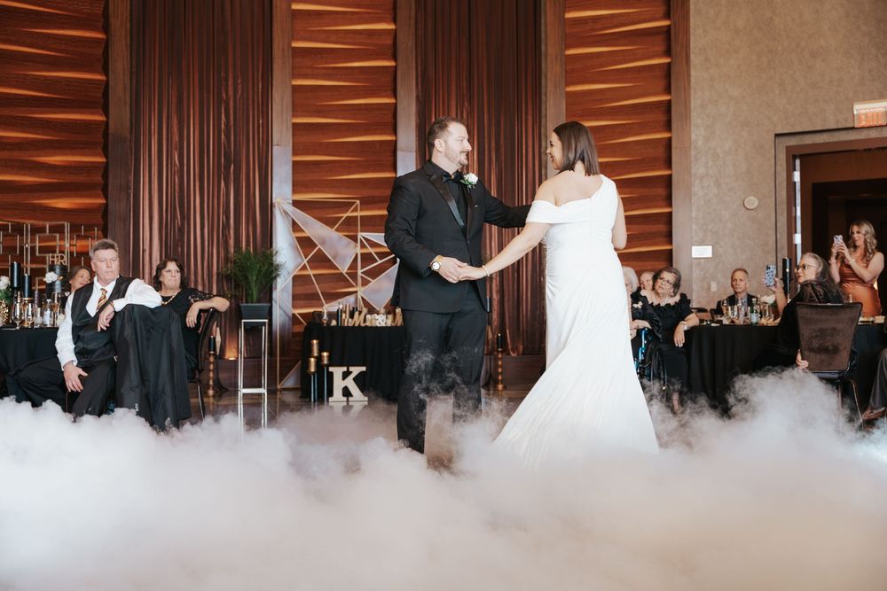 Couple shares their first dance at a wedding reception with fog on the dance floor and wooden paneled walls in the background.