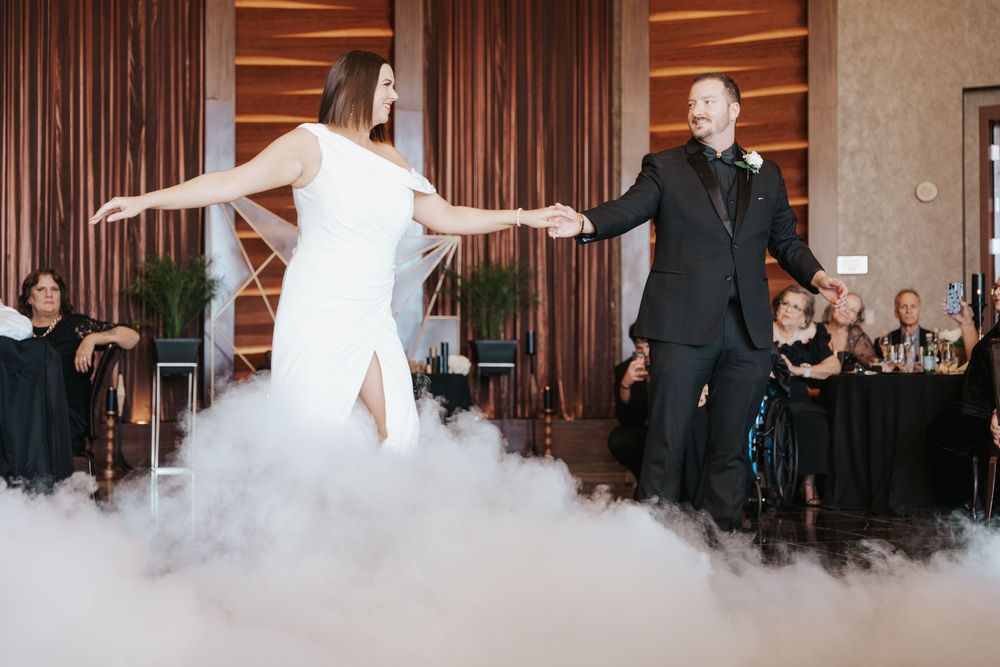A couple performs their first dance at a wedding reception with dramatic fog effects on the dance floor.