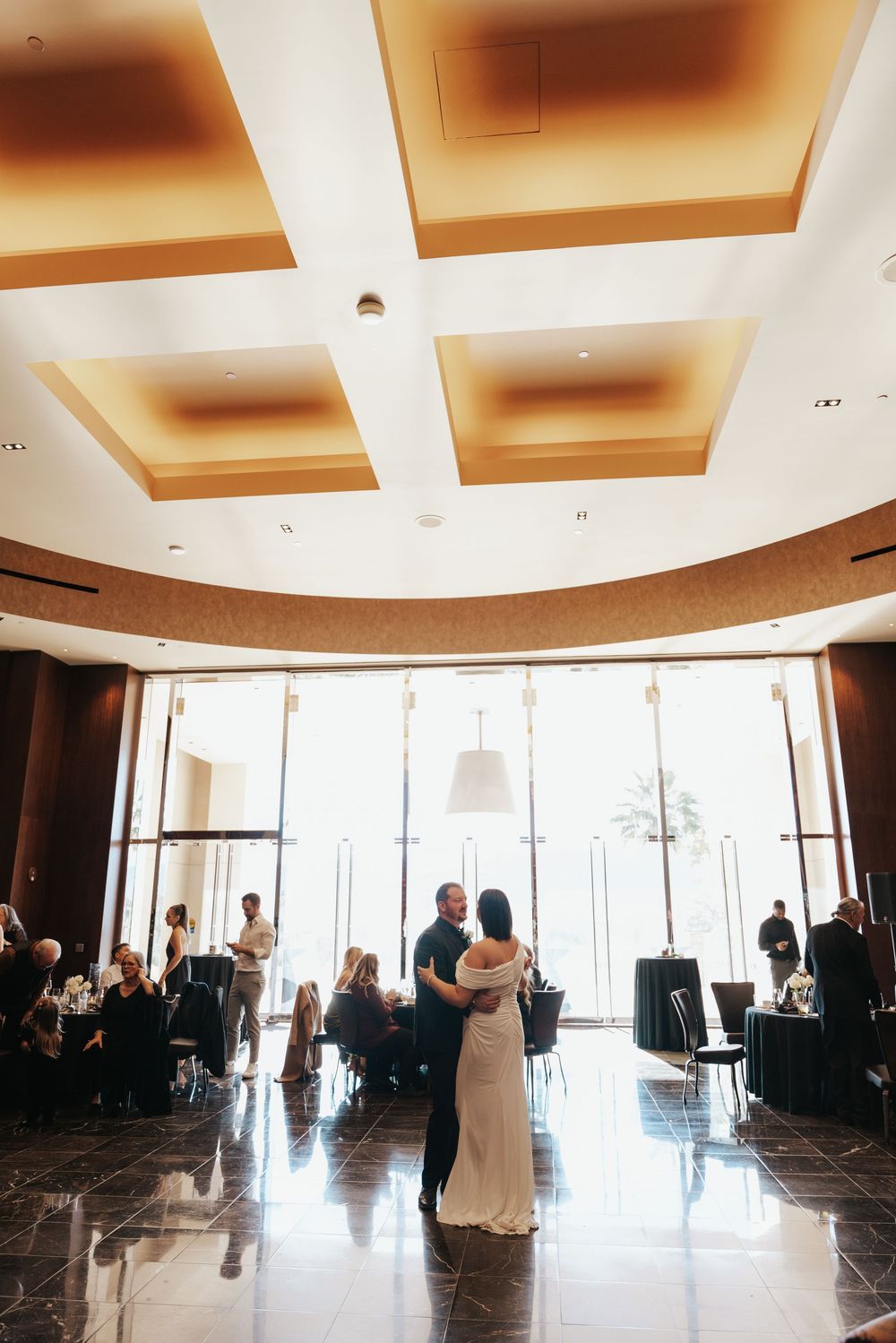 Elegant indoor venue with coffered ceilings and sunlit windows shows guests mingling during an event.