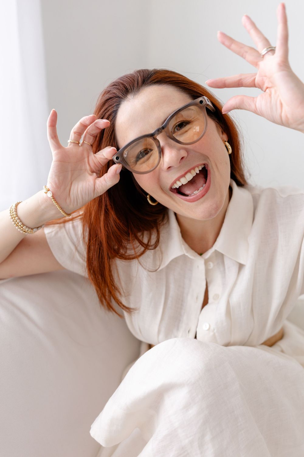 A cheerful person wearing glasses and a white shirt poses with hands near frames while smiling brightly.