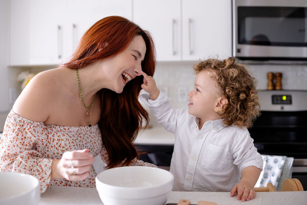A parent and child share a joyful moment while cooking together in a bright modern kitchen.