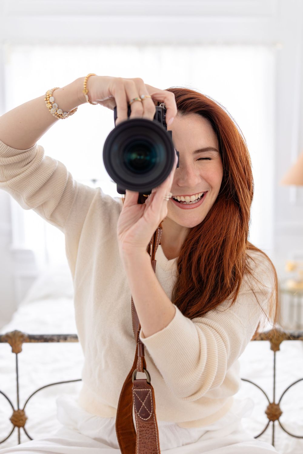 Woman wearing cream sweater takes photos with professional camera in bright interior setting.