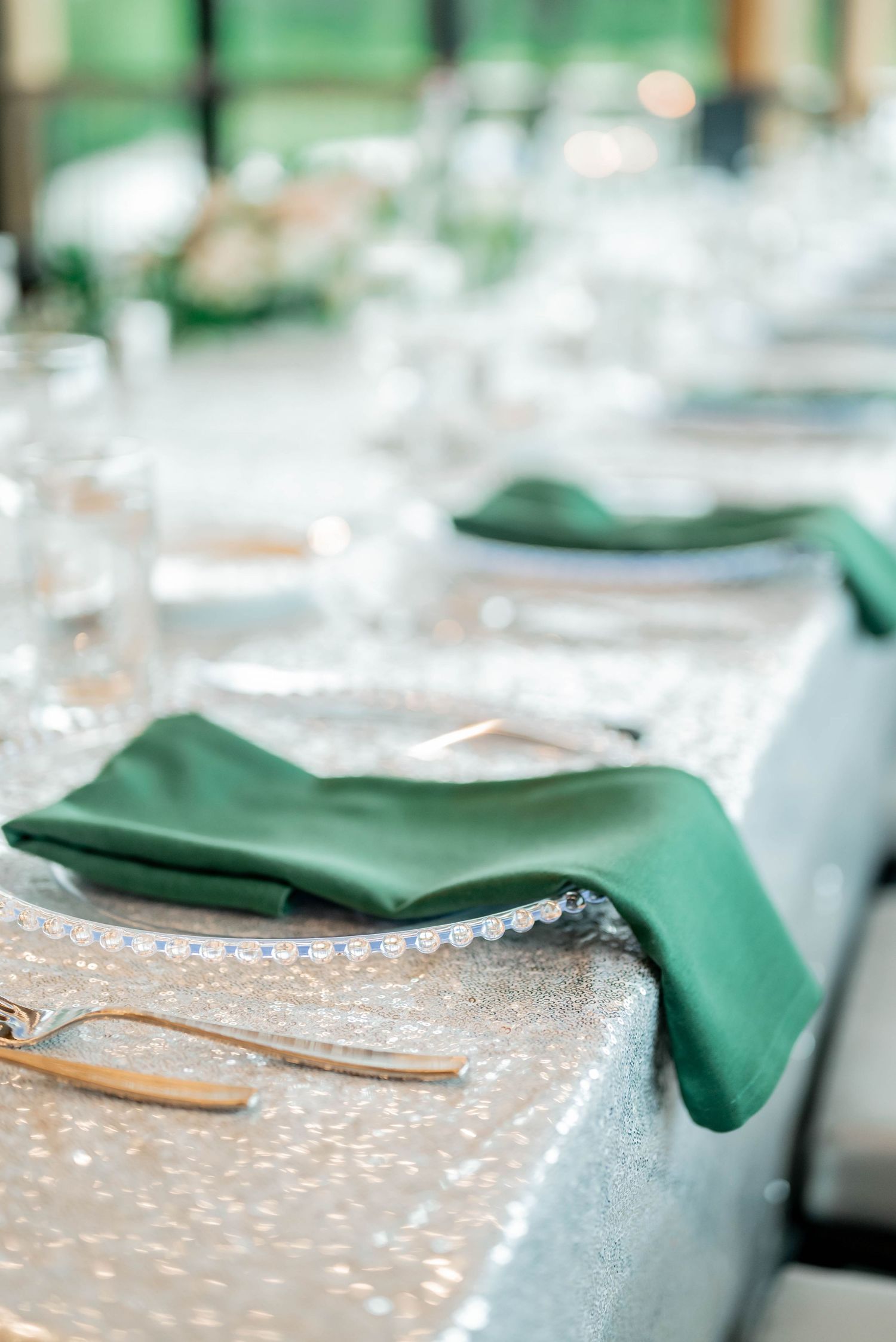Elegant table setting with emerald green napkins on sequin tablecloth with crystal place settings.