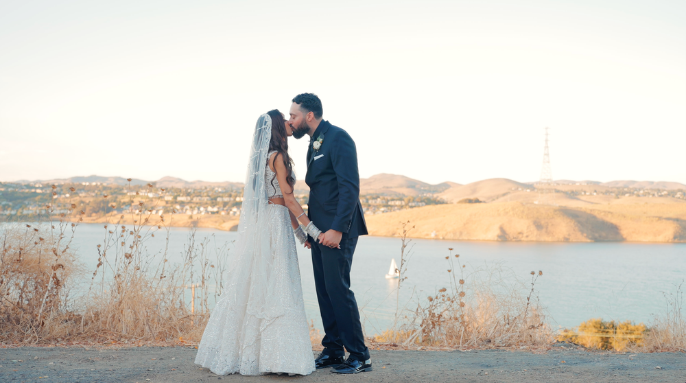 A couple shares a tender moment on a hilltop overlooking a scenic landscape.
