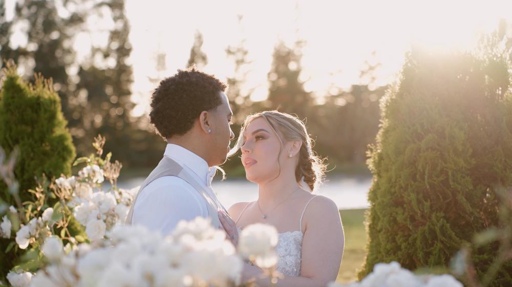 Sunset wedding portrait of couple embracing in garden with golden light filtering through trees.