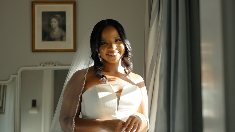 A person in a white dress smiles while standing in soft window light.