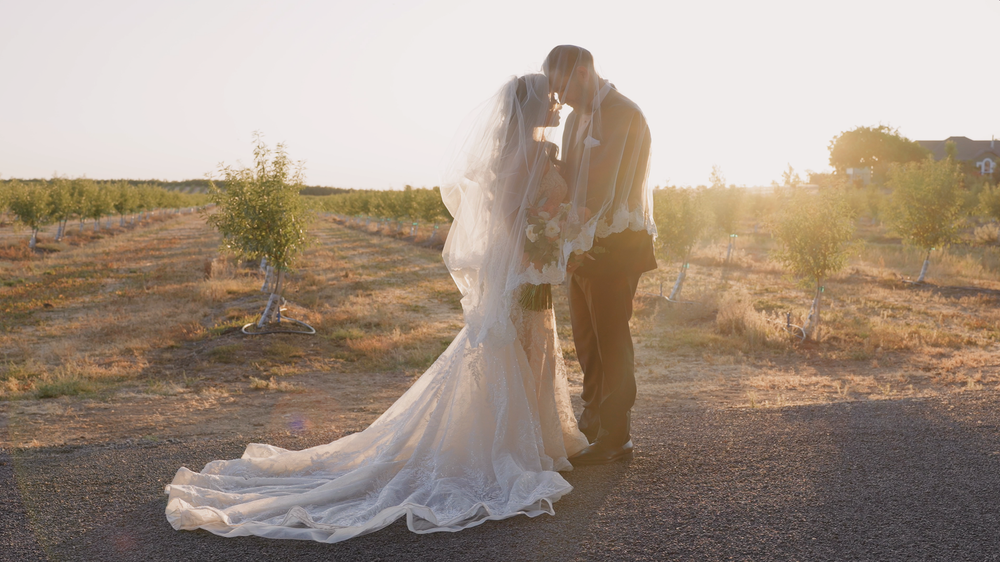 A silhouetted couple shares an intimate moment at sunset in their wedding attire.