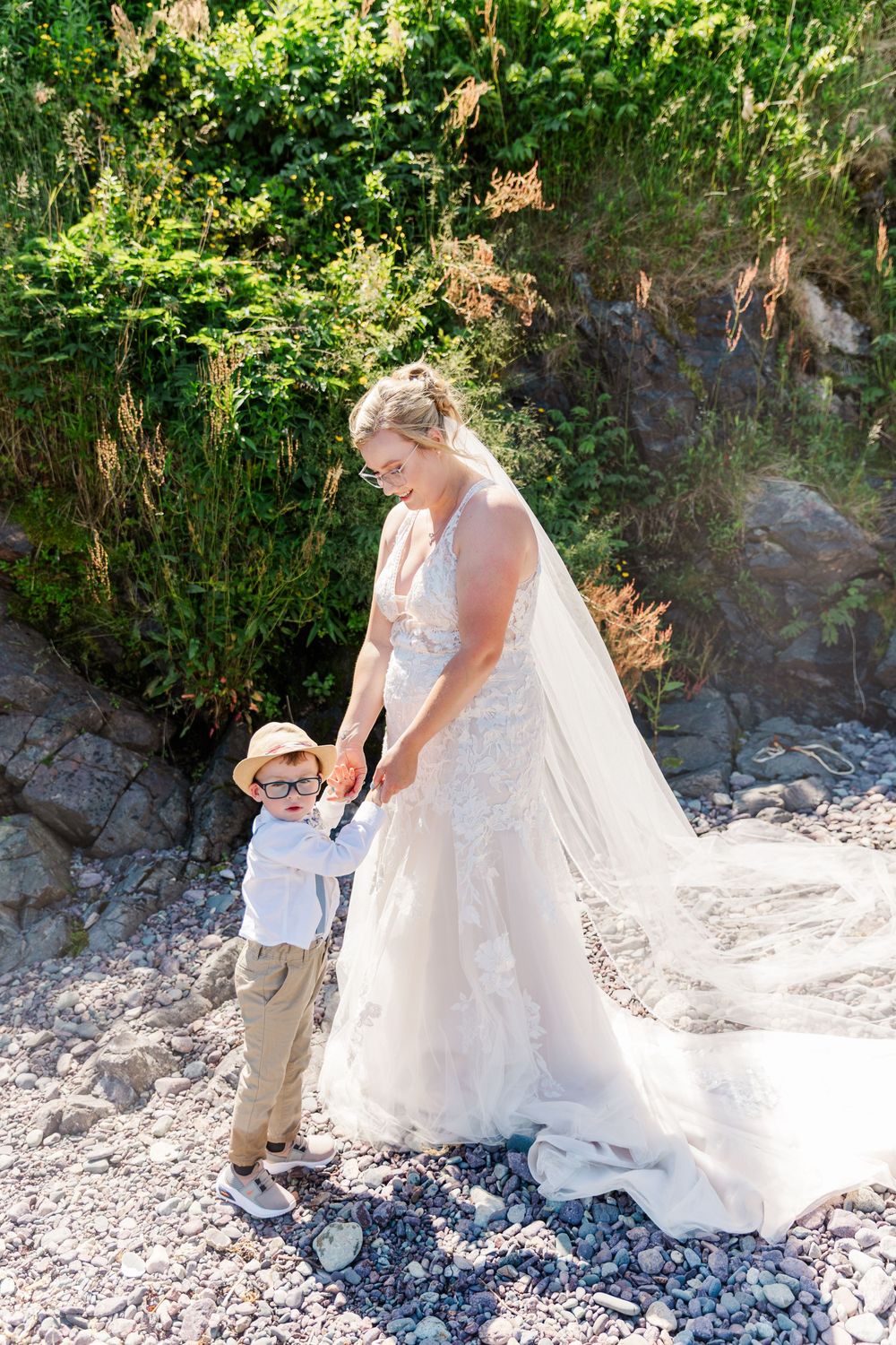 Series of photos showing a bride in a white lace gown interacting with a small child on a rocky beach.