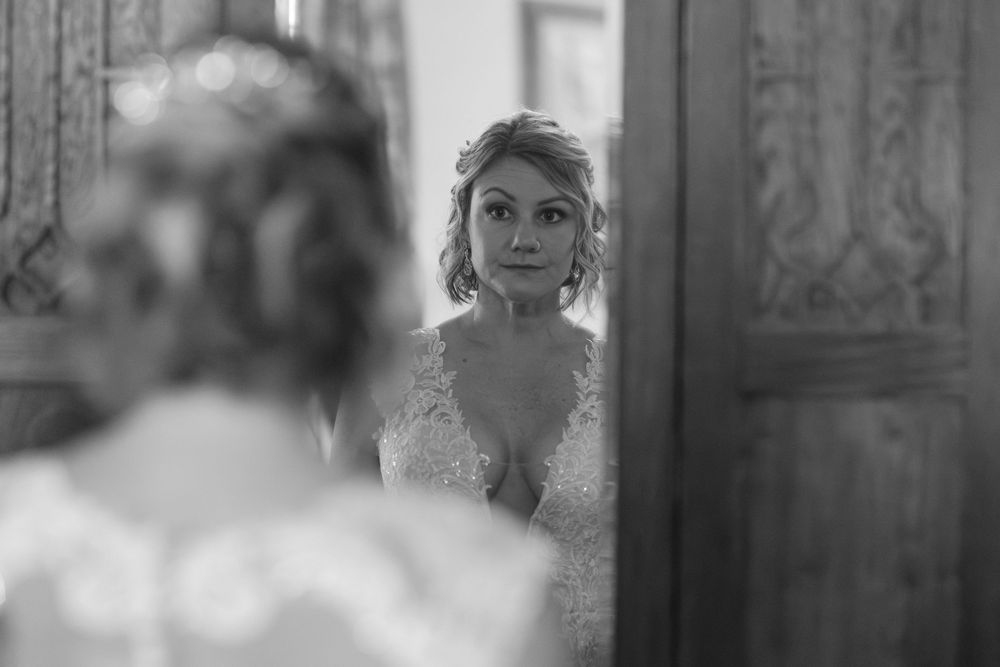 Black and white photo of a bride looking at her reflection in a vintage mirror on her wedding day.