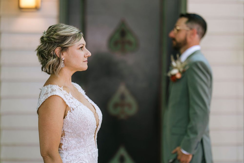 A romantic wedding moment captured with the bride in a lace dress and groom in sage green suit standing apart.