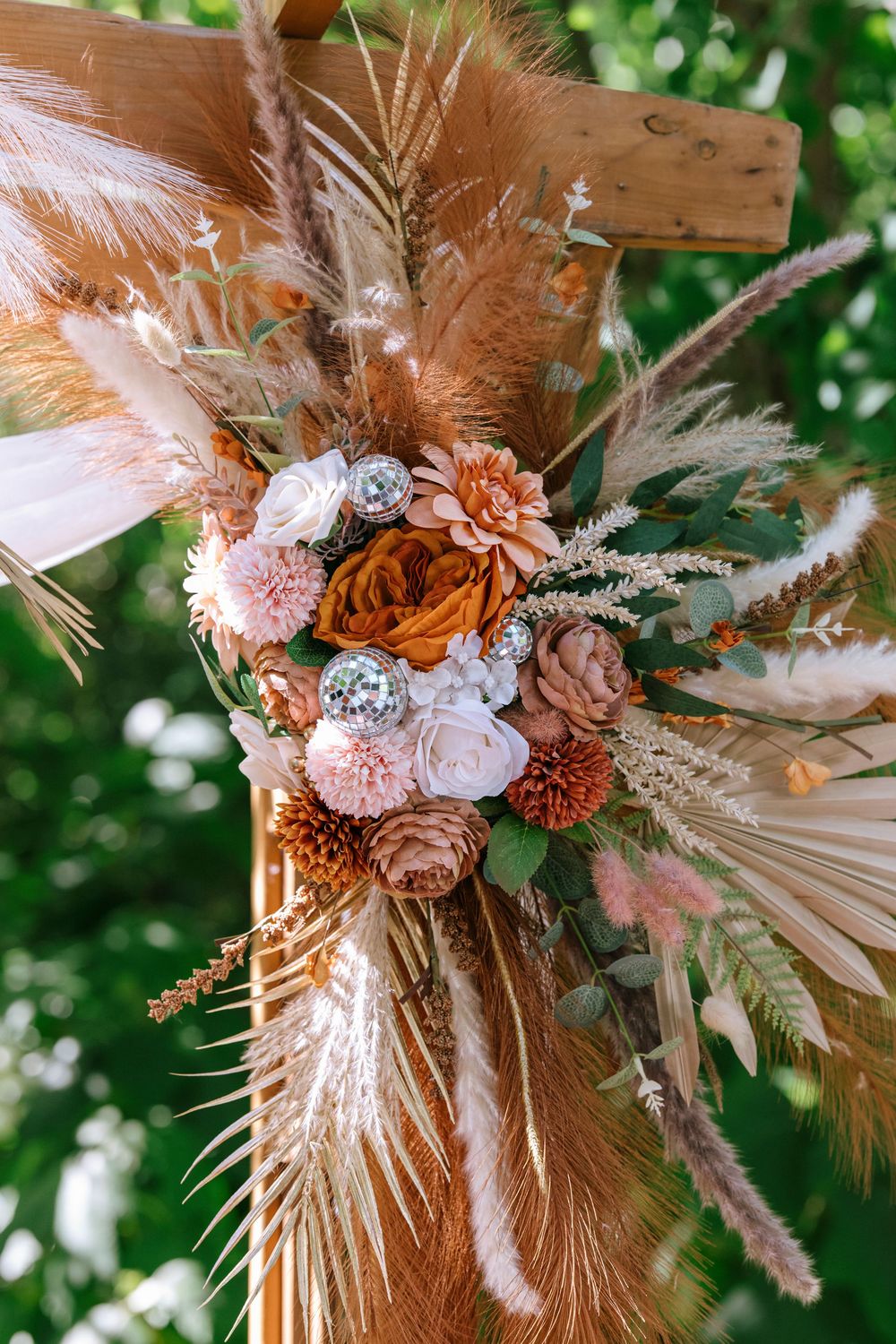 Bohemian floral arrangement with dried palm leaves, pink and orange flowers, and pampas grass against a natural backdrop.