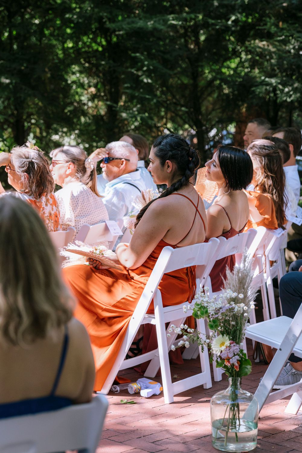 Wedding guests seated in white chairs outdoors share laughter during an emotional moment at a garden ceremony.