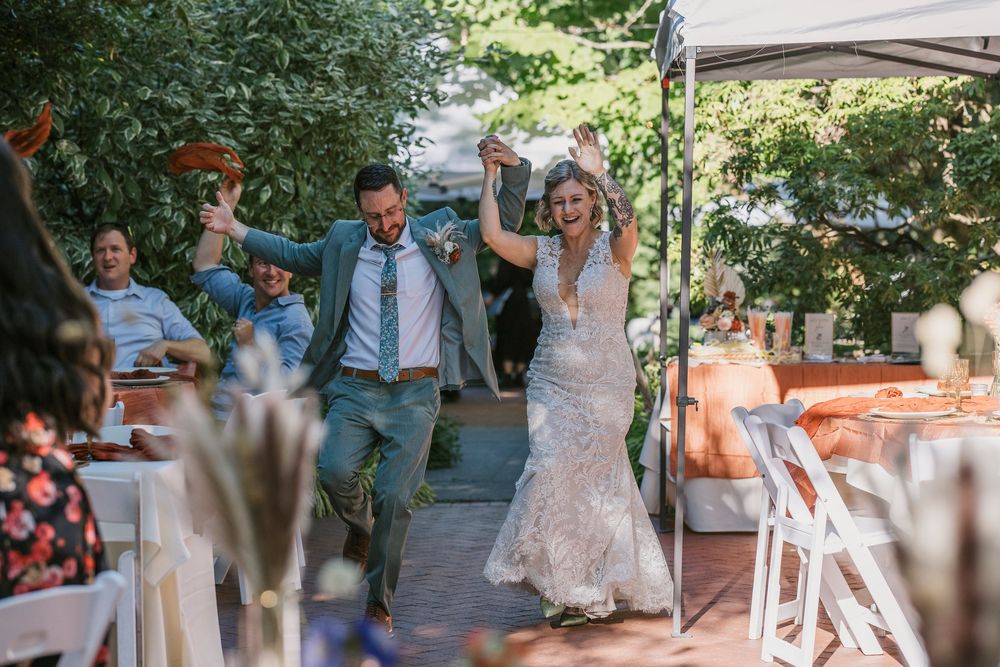 Joyful dance celebration in an outdoor wedding venue with guests forming a circle under green trees and natural lighting.