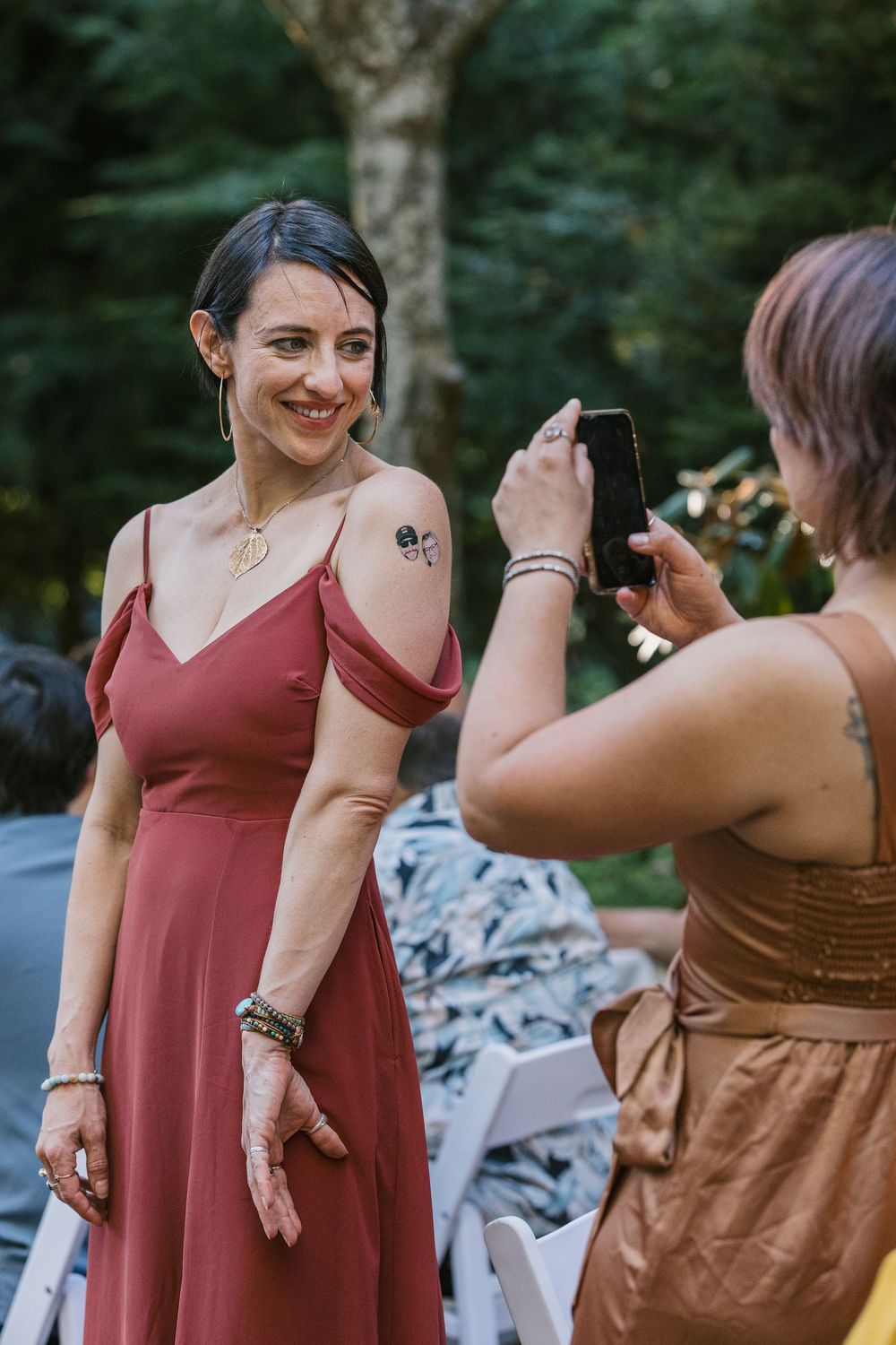 Someone posing in a rose-colored dress while another person takes their photo at an outdoor event.