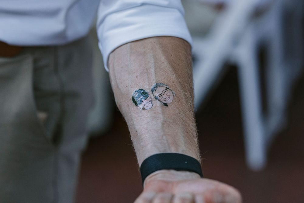 A line of people showing off their tattoos on a light colored background.