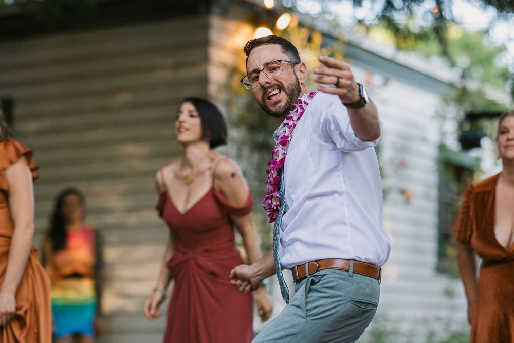 Wedding guests dancing and celebrating outdoors at a festive backyard reception with person in white shirt gesturing joyfully.