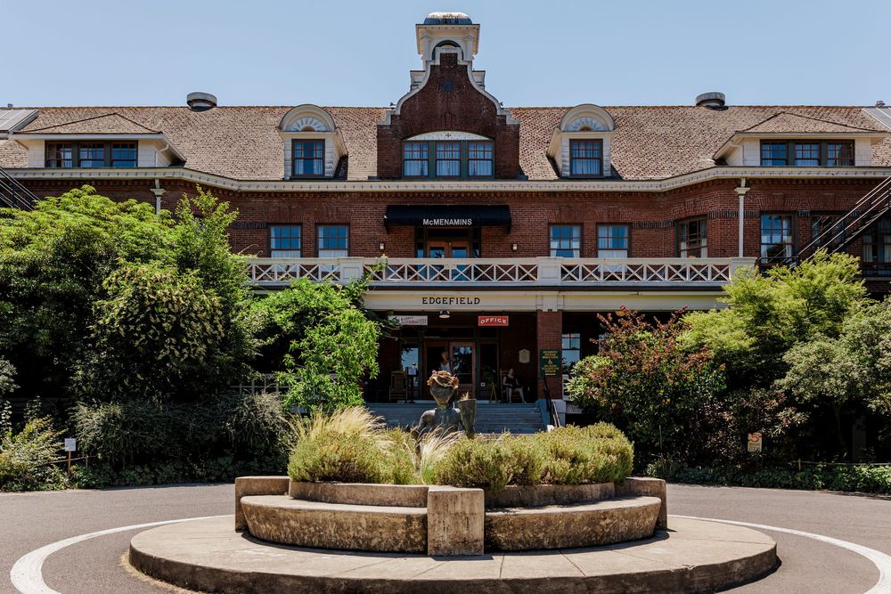 Panoramic view of a grand brick building with a circular courtyard and landscaped gardens.